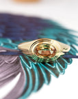 Styled image of a contemporary oval sapphire ring in 14k gold, placed on a brown backdrop. Fine jewelry by Bena Jewelry, made in Montreal.