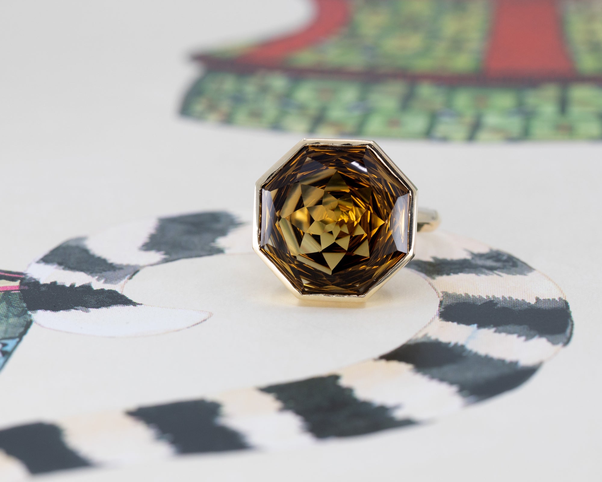 Front view of a large Brazilian dark citrine statement ring, bezel-set in yellow gold, highlighted by a colorful background.