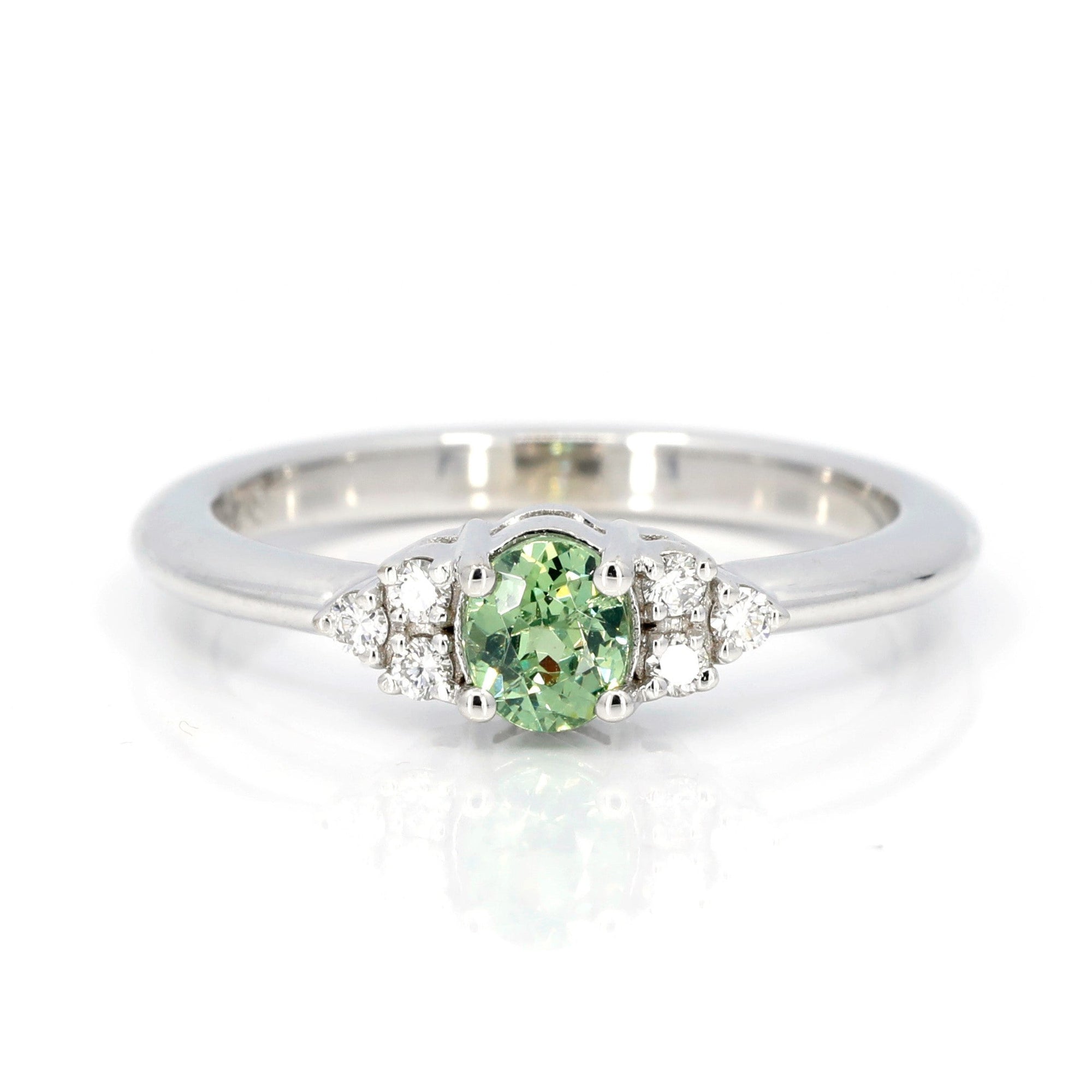 Desir Demantoid Garnet Ring in white gold featuring an oval green garnet and side diamonds by Bena Jewelry photographed on a white background custom-made in Montreal.