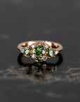 Designer ring with green sapphire and demantoid garnets, set in rose gold, photographed on a bold dark background. Crafted by Bena Jewelry in Montreal.