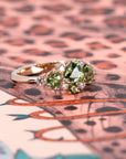 Green sapphire and demantoid garnet ring in rose gold, displayed on a vibrant colored background. Made by Bena Jewelry in Montreal.