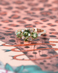 Custom designer ring with green gemstones in rose gold, shown against a soft-colored backdrop. Created by Bena Jewelry, Montreal, Canada.