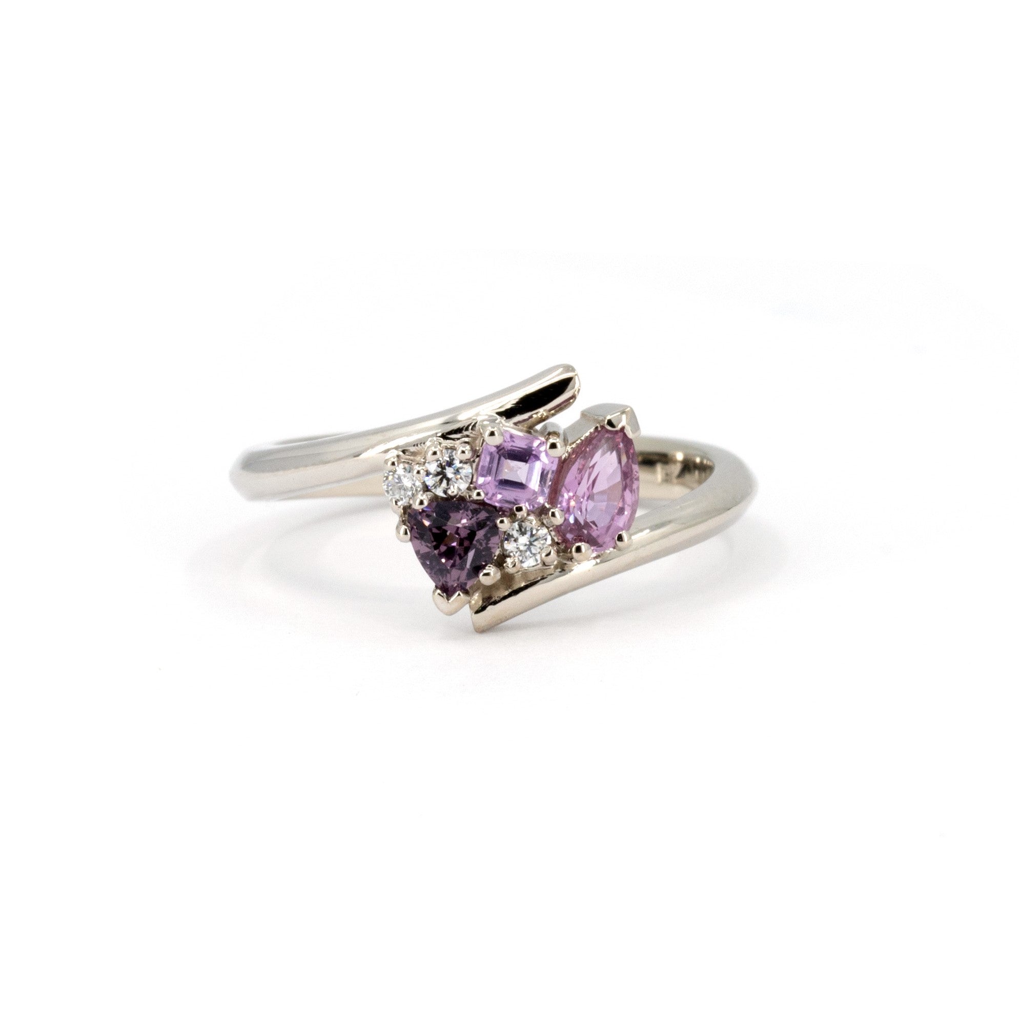 White gold Kink Avalanche ring by Bena Jewelry, featuring purple and pink sapphires in trillion, pear, and round diamond cuts, with a dynamic twist band design, displayed on a white background.