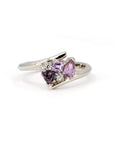 White gold Kink Avalanche ring by Bena Jewelry, featuring purple and pink sapphires in trillion, pear, and round diamond cuts, with a dynamic twist band design, displayed on a white background.