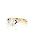 Yellow gold engagement ring with a central marquise-cut diamond, flanked by sparkling diamonds and royal blue sapphires, handcrafted by Bena Jewelry, displayed on a white background.