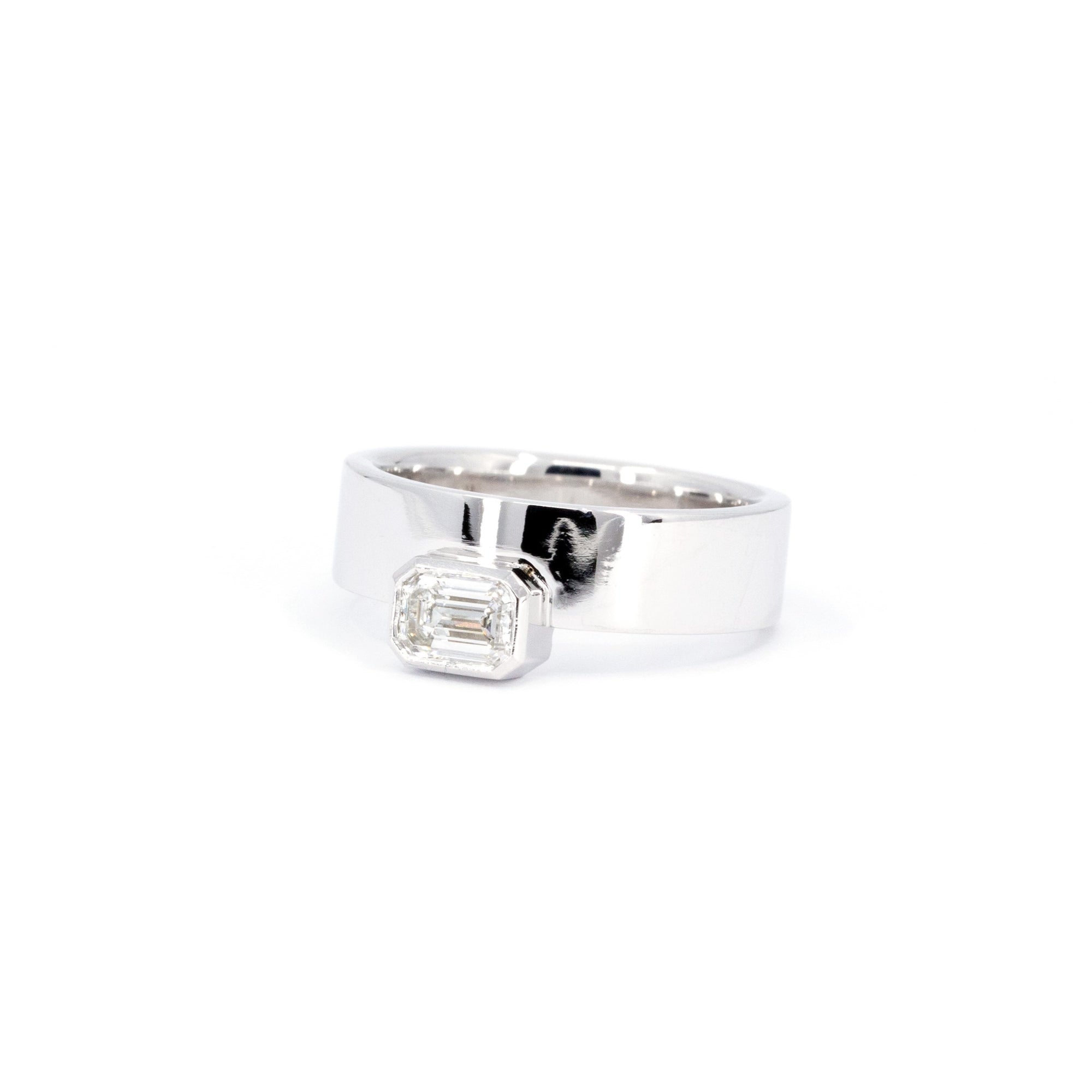 White gold unisex ring with emerald-cut diamond in bezel setting, designed by Bena Jewelry. Bold and boxy design, perfect for making a statement in modern fine jewelry.