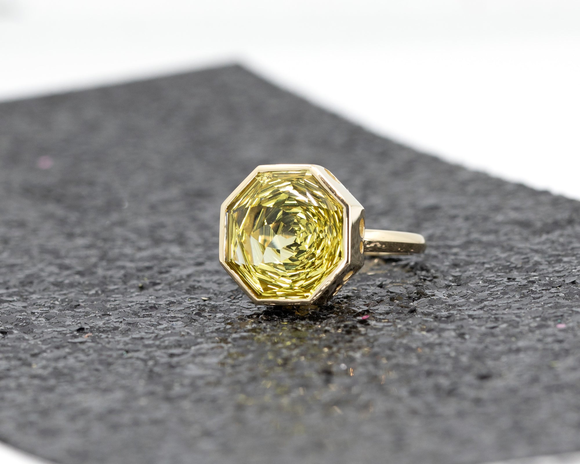 Lemon quartz ring in yellow gold with a bold octagonal cut, shimmering against a dark glittering backdrop.
