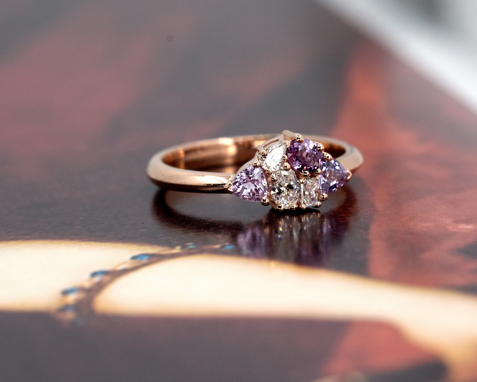 Side view of the Avalanche ring, showcasing the unique arrangement of pink and purple sapphires and diamonds in 14 kt rose gold.