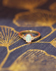 front view of oval shape opal gemstone and diamond on yellow gold engagement ring by bena jewelry on multi color background