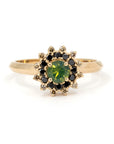 Bena Jewelry ring designed in Montreal, featuring a round opalescent green sapphire with a starburst halo of black and brown diamonds, set in 14k yellow gold on a white background.