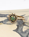Artistic shot of a Bena Jewelry green sapphire and diamond ring on a colorful backdrop, showcasing the contrast of black and brown diamonds against 14k gold, made in Montreal.