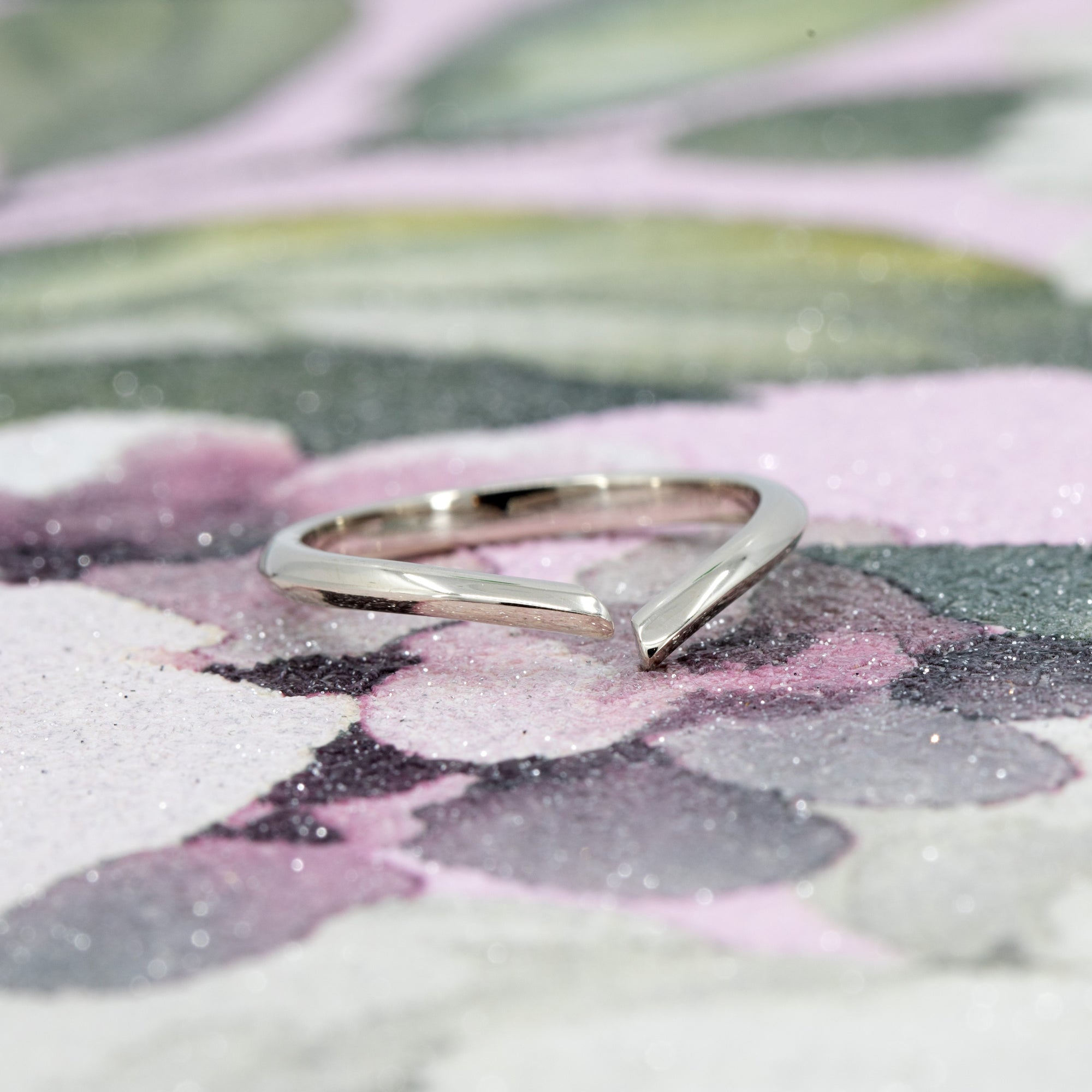Minimalist open band ring in white gold, photographed on a warm-toned background. The ring’s sleek, curved design and high polish create a refined, modern look.