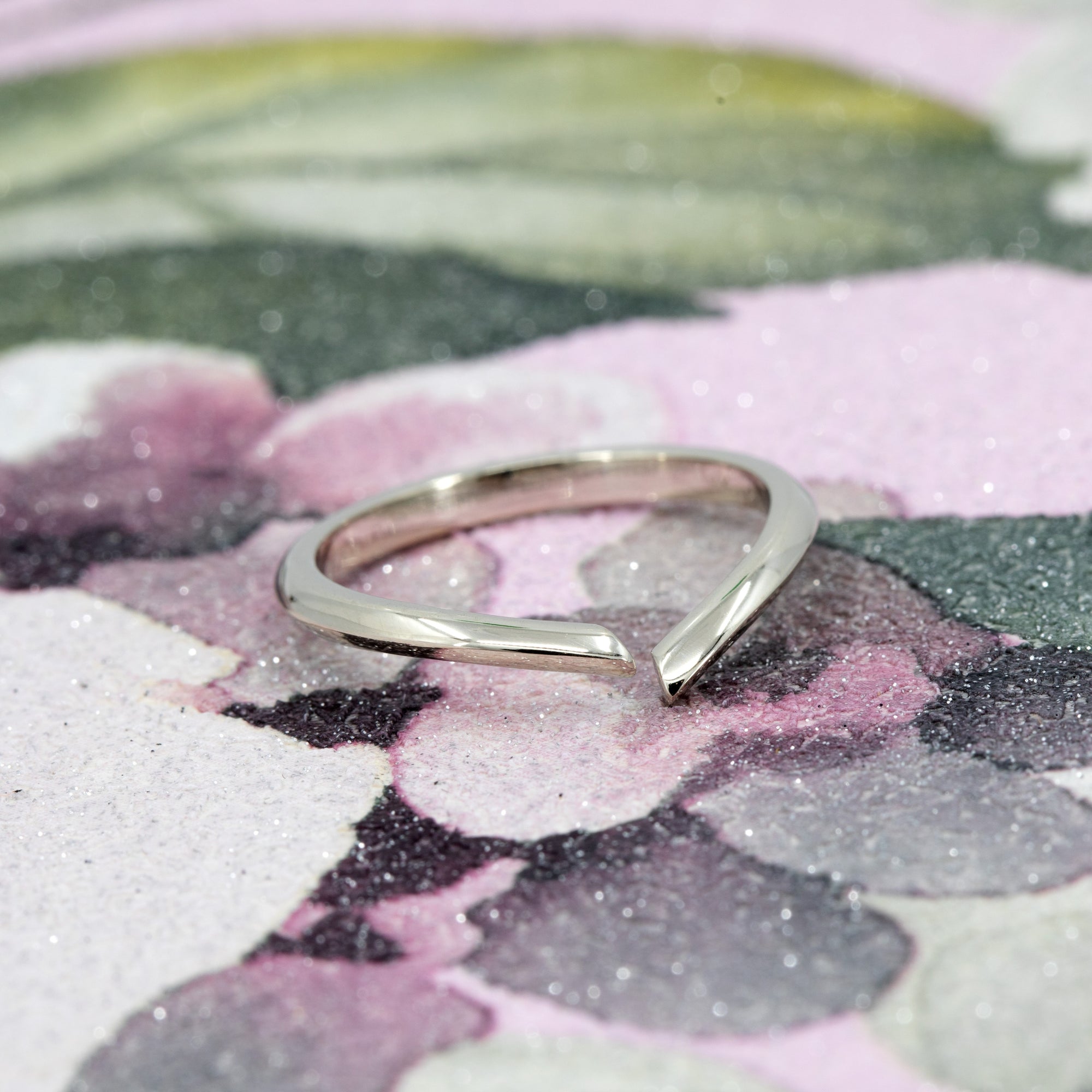 Artistic shot of the Sleek Gap Ring in 14k white gold. The open-ended structure and contemporary silhouette stand out against a bold, contrasting background.