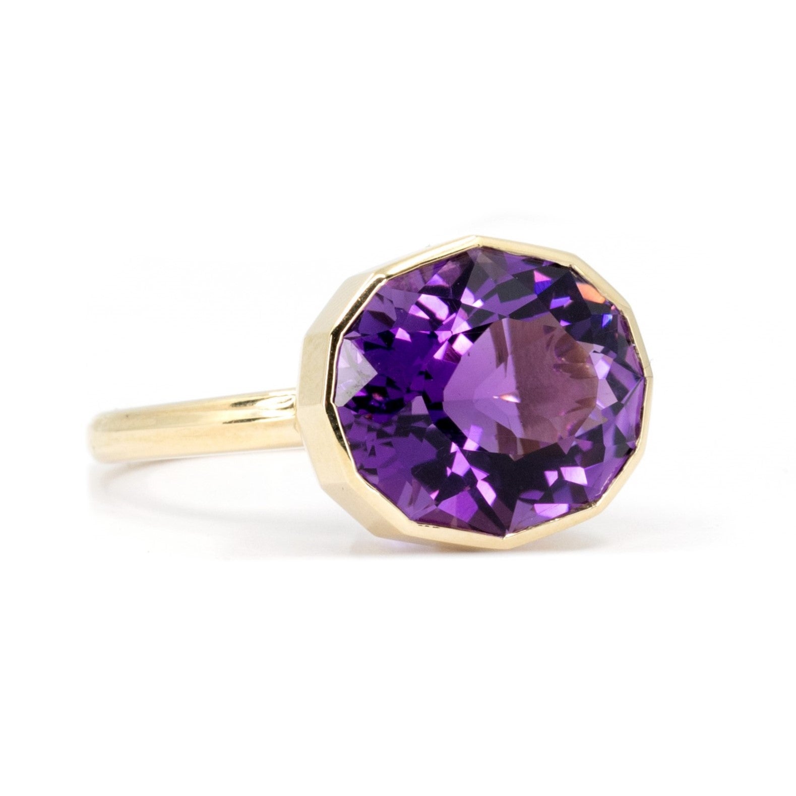 Side view Oval octagonal amethyst ring in yellow gold with deep purple hues and pink accents, displayed on a white background.