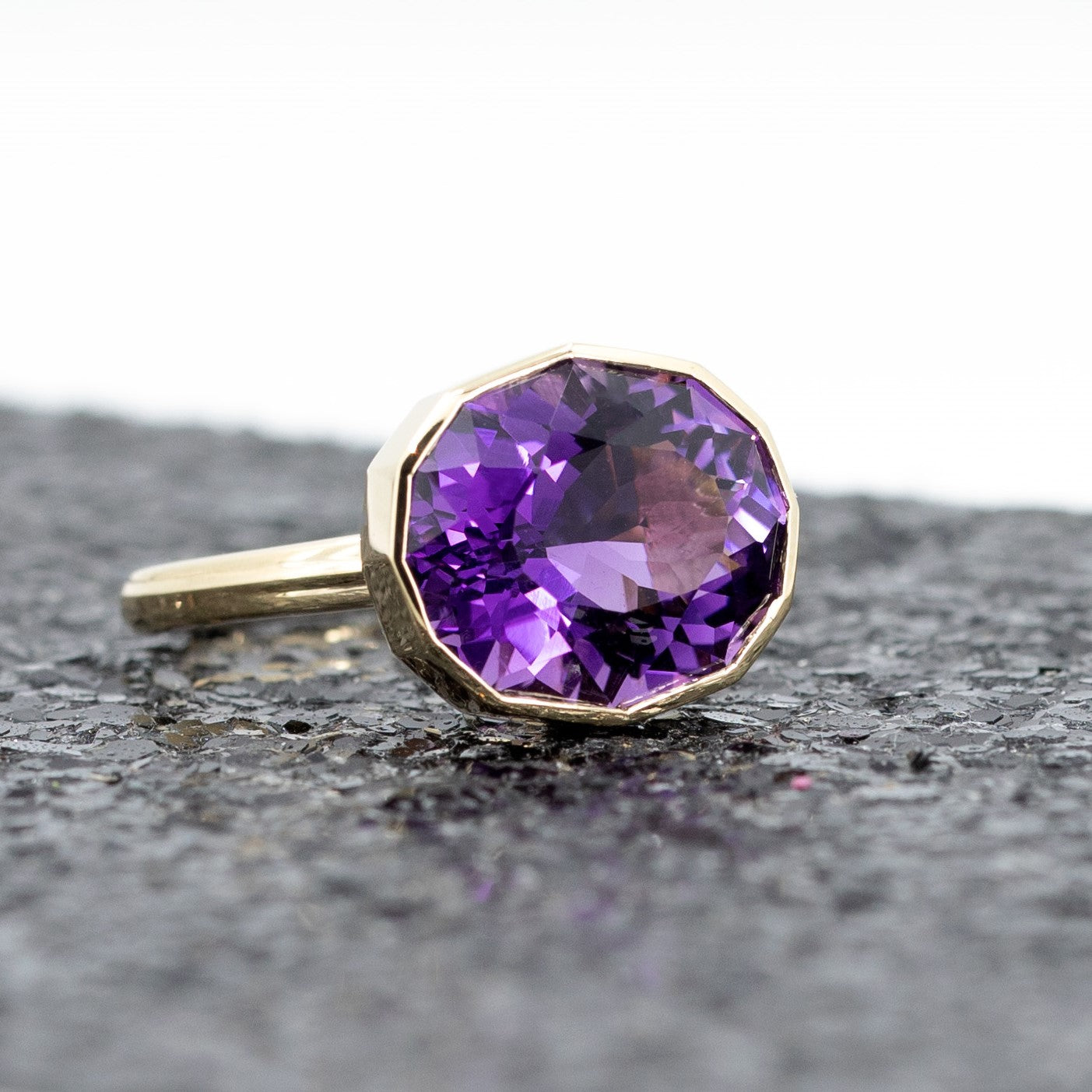 Side view of Bena Jewelry deep purple and pink Brazilian amethyst cocktail ring, set in yellow gold, highlighted by a glitter backdrop.