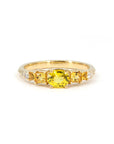Yellow gold engagement ring by Bena Jewelry, featuring a vivid yellow oval sapphire center stone, flanked by orange princess cut sapphires and diamonds, displayed on a white background.