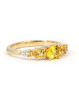 Close-up of Bena Jewelry's yellow gold engagement ring, highlighting the vivid yellow oval sapphire center stone, orange princess cut sapphires, and diamond accents, set against a white background.
