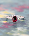 Vivid ruby ring in minimalist white gold setting, shown on a textured colored surface, Canadian fine jewelry by Bena Jewelry.