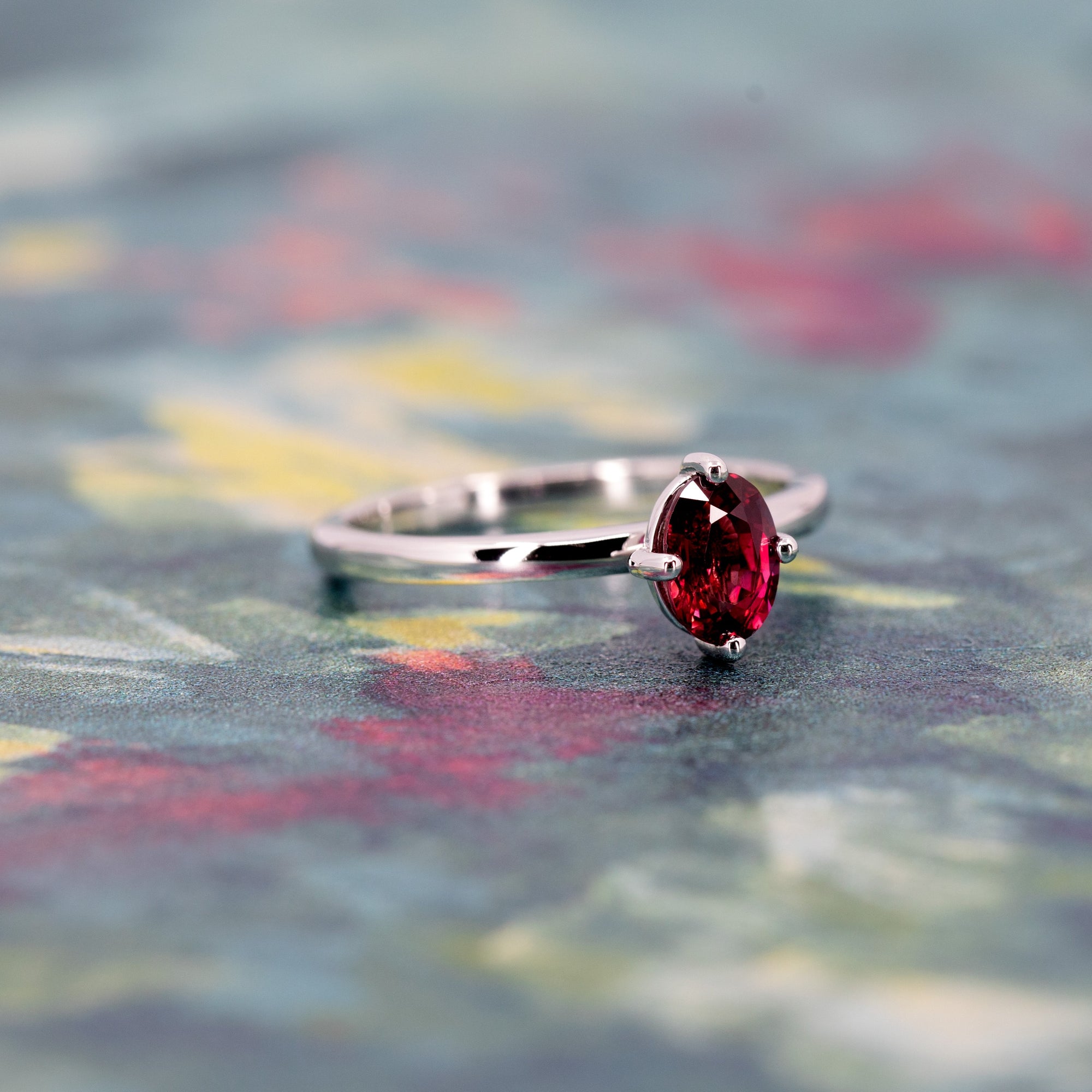 Oval ruby solitaire ring in white gold displayed on a warm-toned background, designed by Bena Jewelry in Montreal.