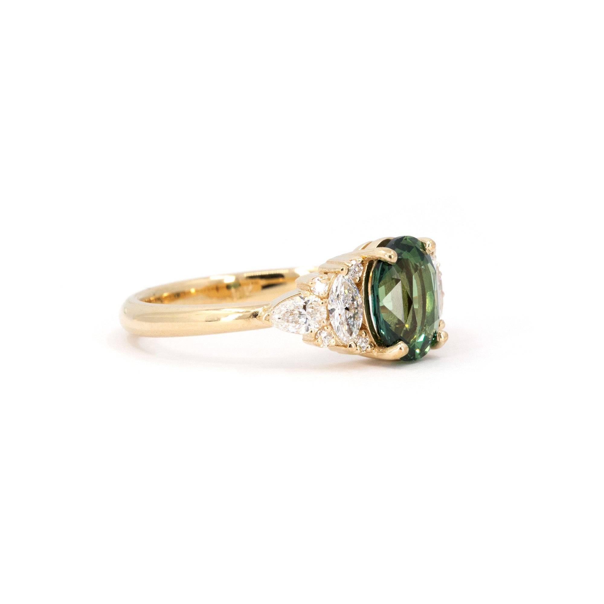 Close-up of sapphire and diamond ring on dark background – The vivid teal sapphire and diamonds stand out dramatically in this custom-designed fine jewelry piece.