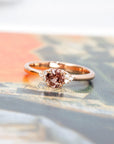 The Désir Peach Spinel Ring set against a warm-toned background, highlighting its cushion-cut gemstone and rose gold setting. A refined creation by Bena Jewelry.
