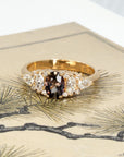 Artistic shot of a handcrafted engagement ring with oval peacock sapphire and mixed-cut diamonds, designed by Bena Jewelry in Montreal, set against a moody colored background.