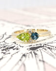 Close-up of the ring worn, showing the interplay of green and blue gemstones – A unique engagement ring crafted by Bena Jewelry in Montreal.