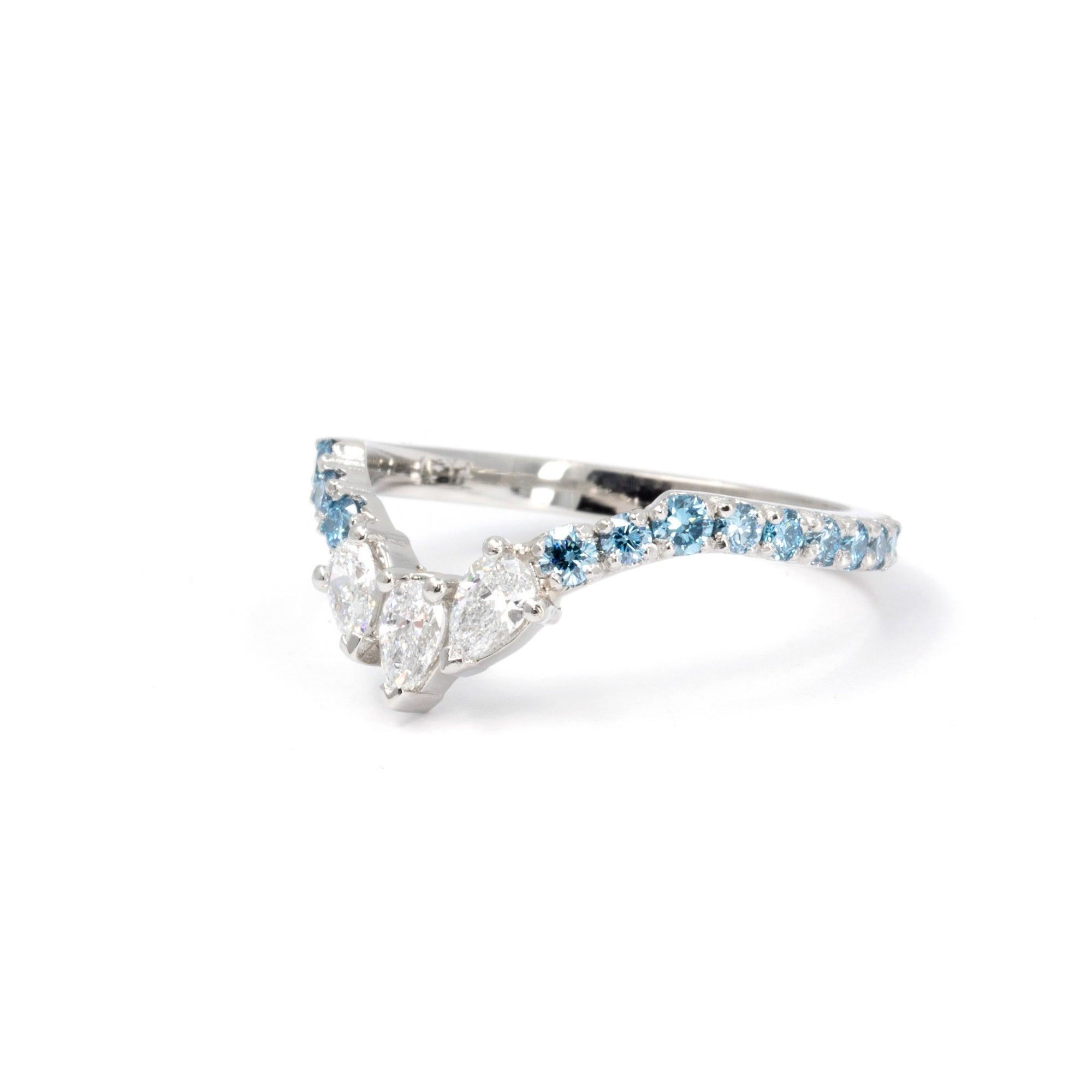 Platinum ring with three pear-cut white diamonds and a row of round blue diamonds, designed by Bena Jewelry in Montreal.