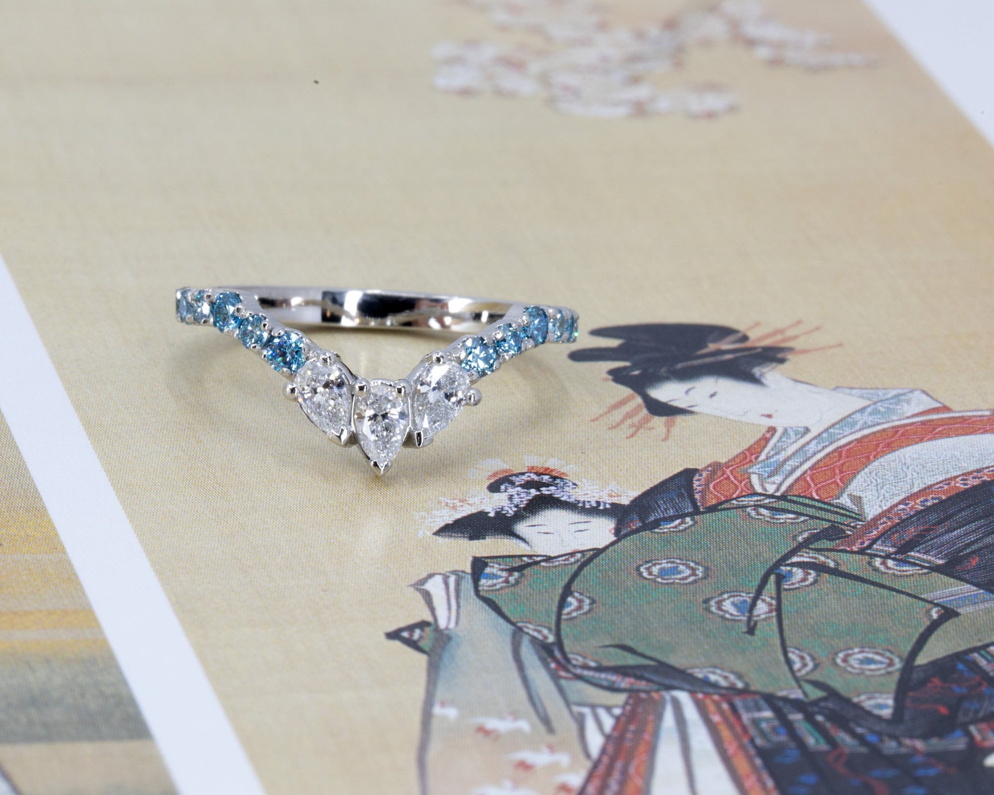 Lifestyle image of the Blue Mirage platinum ring with blue and white diamonds, glowing softly against a colored surface.
