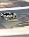 Elegant pinch-designed platinum wedding ring with sparkling diamonds, set against a bold colored backdrop. Crafted by Bena Jewelry, Montreal, Canada.