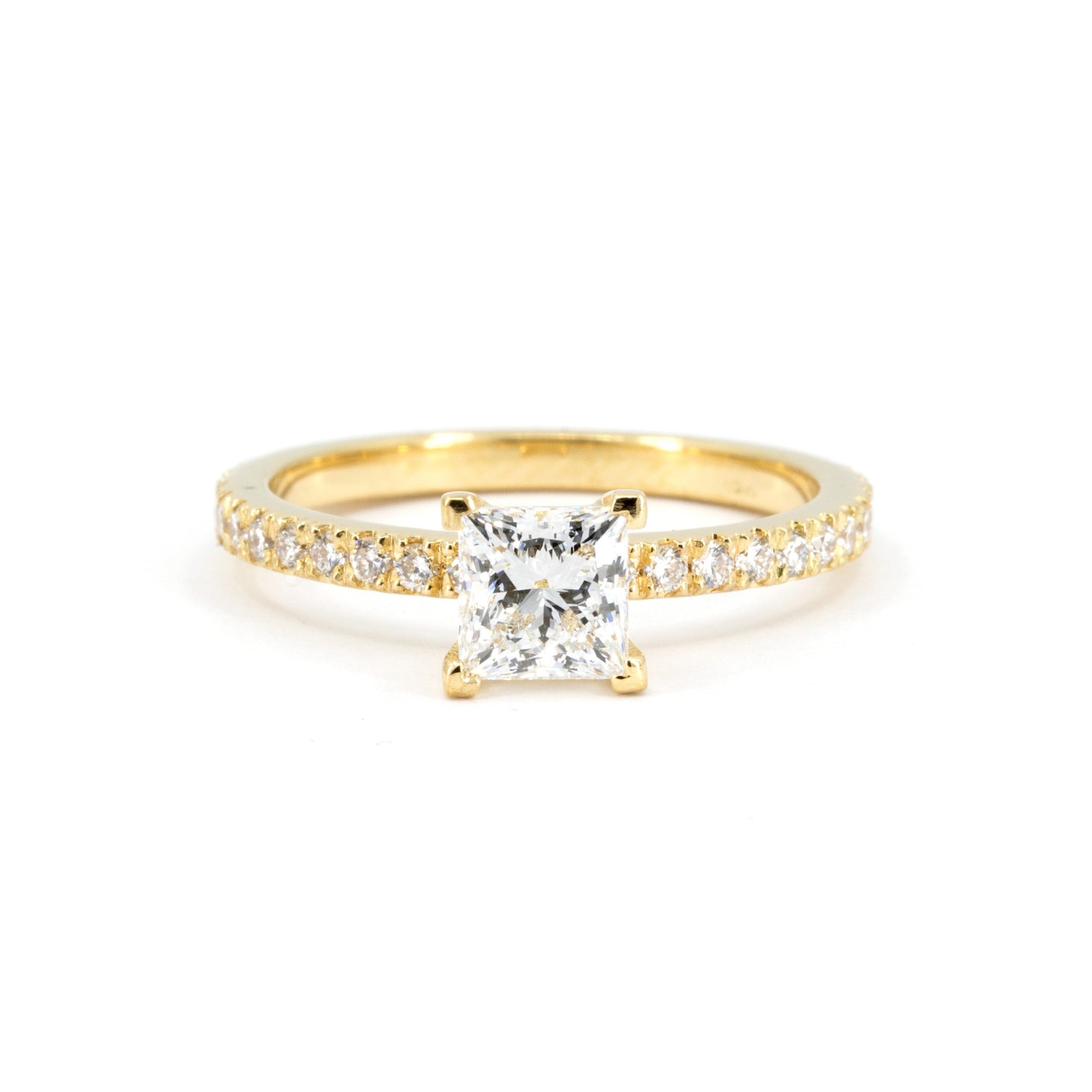 Close-up of a princess-cut diamond engagement ring in yellow gold with pavé-set diamonds on a white background, made by Bena Jewelry in Montreal, Canada.