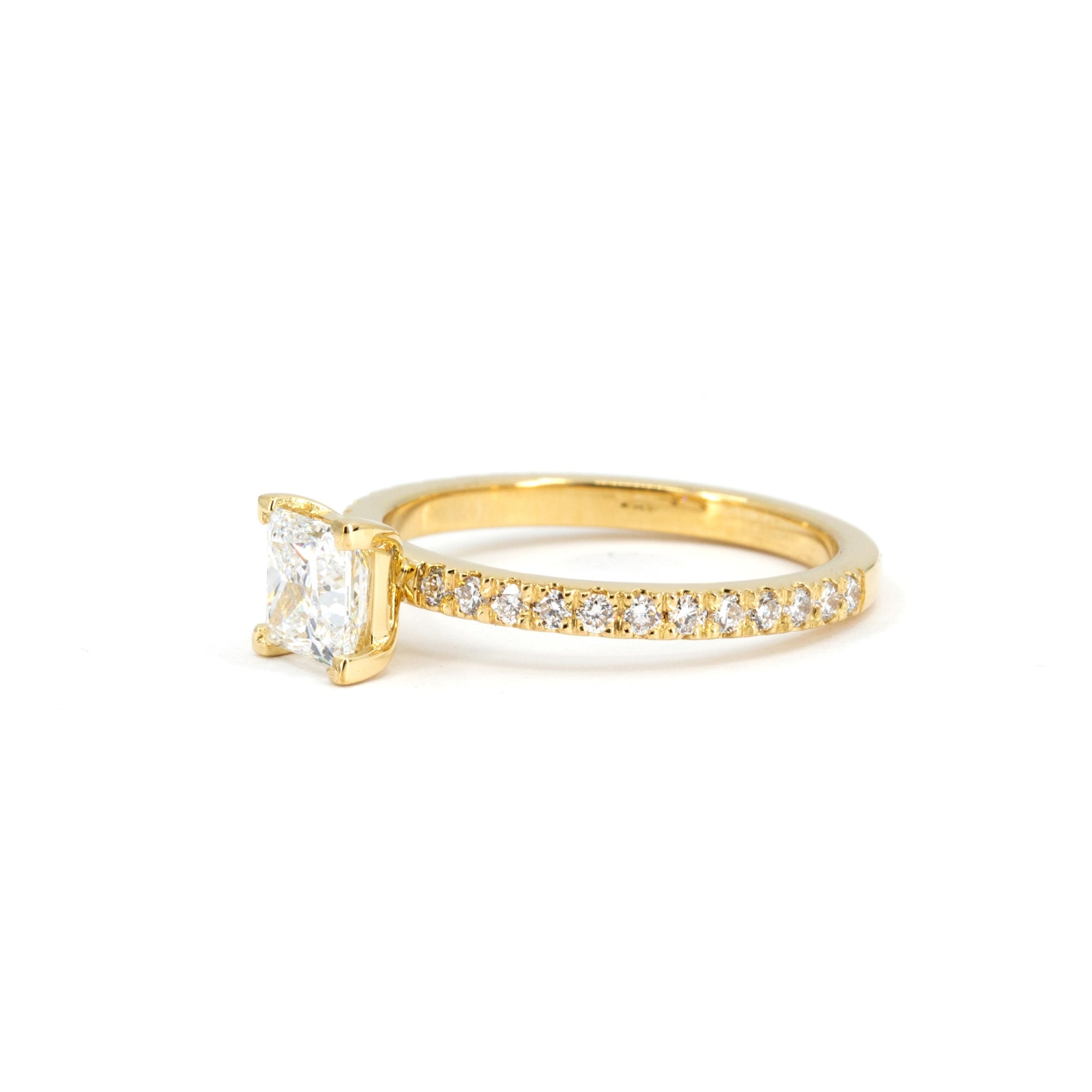 Side view of Bena Jewelry yellow gold ring featuring a central princess-cut diamond and diamond pavé band, photographed on white.