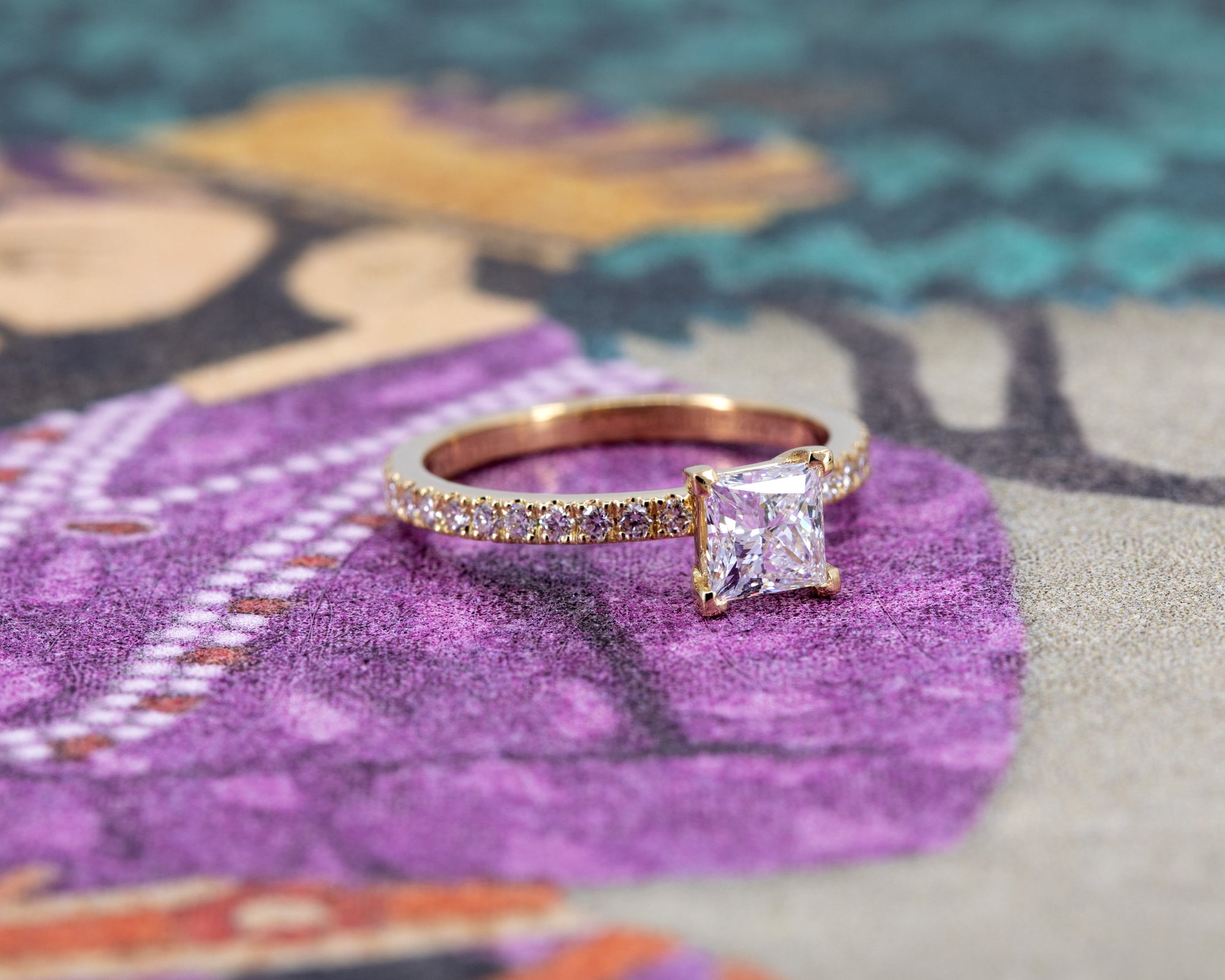 Contemporary engagement ring in 18k yellow gold with diamond pavé, designed by Bena Jewelry, shown against a muted color background.