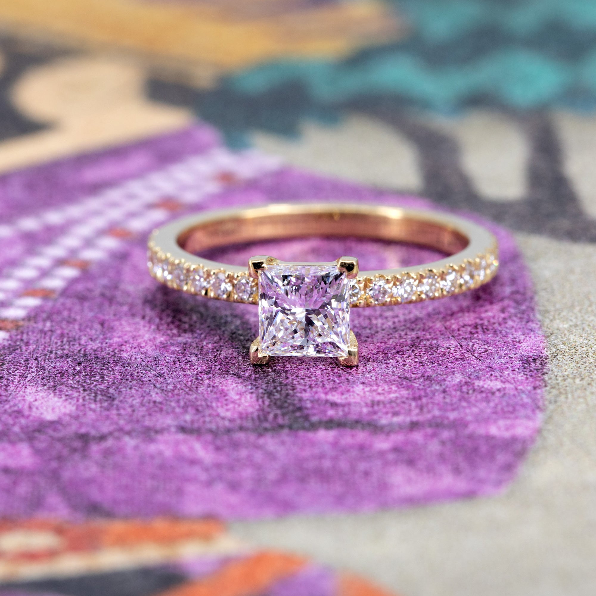 Elegant yellow gold diamond ring with a princess-cut center stone by Bena Jewelry, styled on a soft colored backdrop.