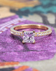 Elegant yellow gold diamond ring with a princess-cut center stone by Bena Jewelry, styled on a soft colored backdrop.