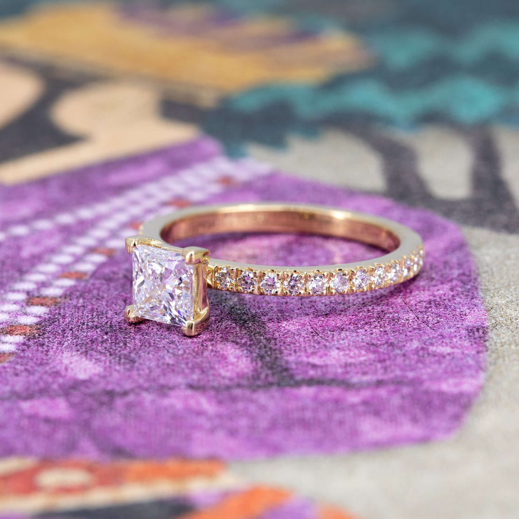 Bena Jewelry engagement ring with princess-cut diamond and pavé band in yellow gold, displayed on a warm-toned background, handmade in Montreal.