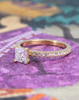 Bena Jewelry engagement ring with princess-cut diamond and pavé band in yellow gold, displayed on a warm-toned background, handmade in Montreal.