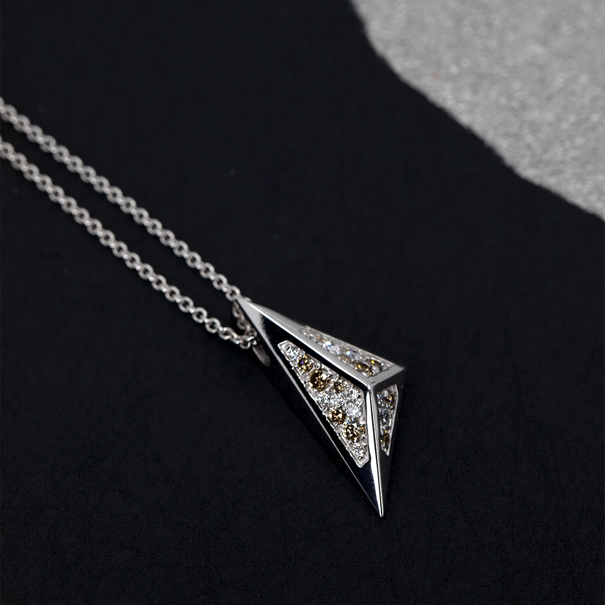 Bold geometric pendant in white gold, featuring golden-brown and white diamonds, glowing against a dark backdrop. Handmade in Montreal by Bena Jewelry.