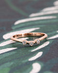 Rose gold wedding band with three white diamonds, set against a rich-colored background. A contemporary and timeless design by Bena Jewelry.