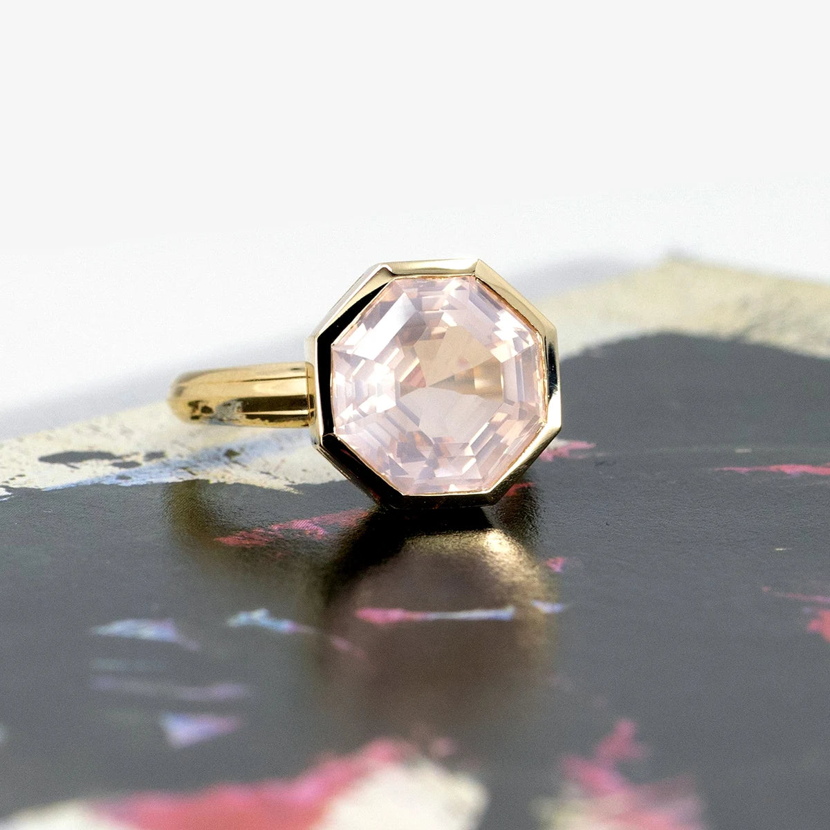 Front view of a rose quartz statement ring, bezel-set in yellow gold, highlighted on a bold colorful background.