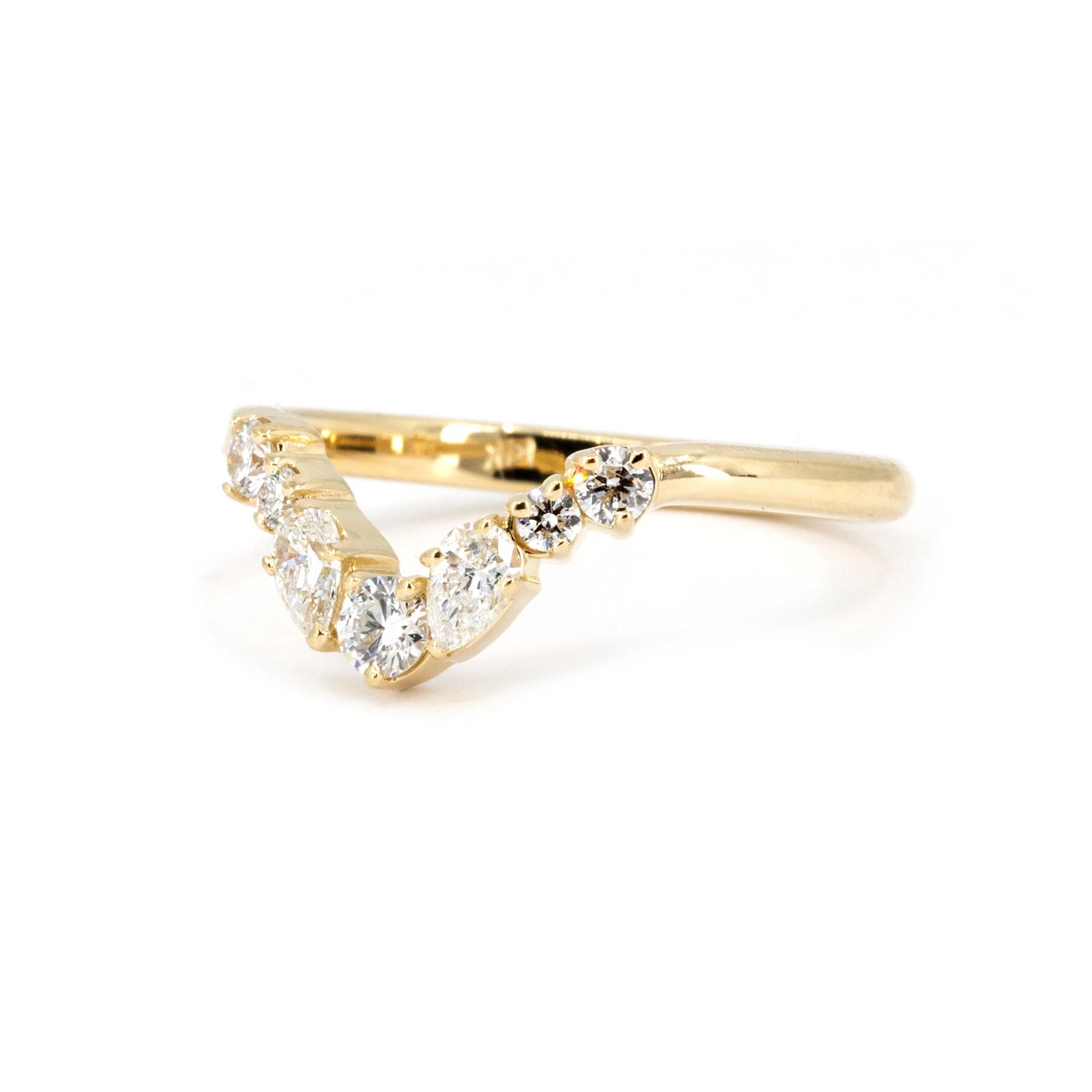 Side view of a yellow gold diamond wedding band by Bena Jewelry, highlighting its sleek profile with round and pear-shaped diamonds. Photographed against a white background.