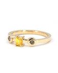 Minimalist shot of a handcrafted yellow gold ring with a central yellow emerald-cut diamond and two side brown diamonds, set in bezel settings, displayed on a white background.