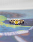 Elegant close-up of a handcrafted gold ring with a yellow diamond centerpiece and brown diamonds, photographed on a contrasting color background.