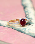Close-up of the center stone: Oval ruby in a white gold prong setting on a yellow gold ring with pavé diamonds, crafted in Montreal by Bena Jewelry.