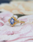 y Bloom Oval Sapphire Ring worn on hand, close-up – A unique engagement ring featuring a sky-blue oval sapphire with an organic, floral-inspired gold design. Handmade by Bena Jewelry in Montreal.