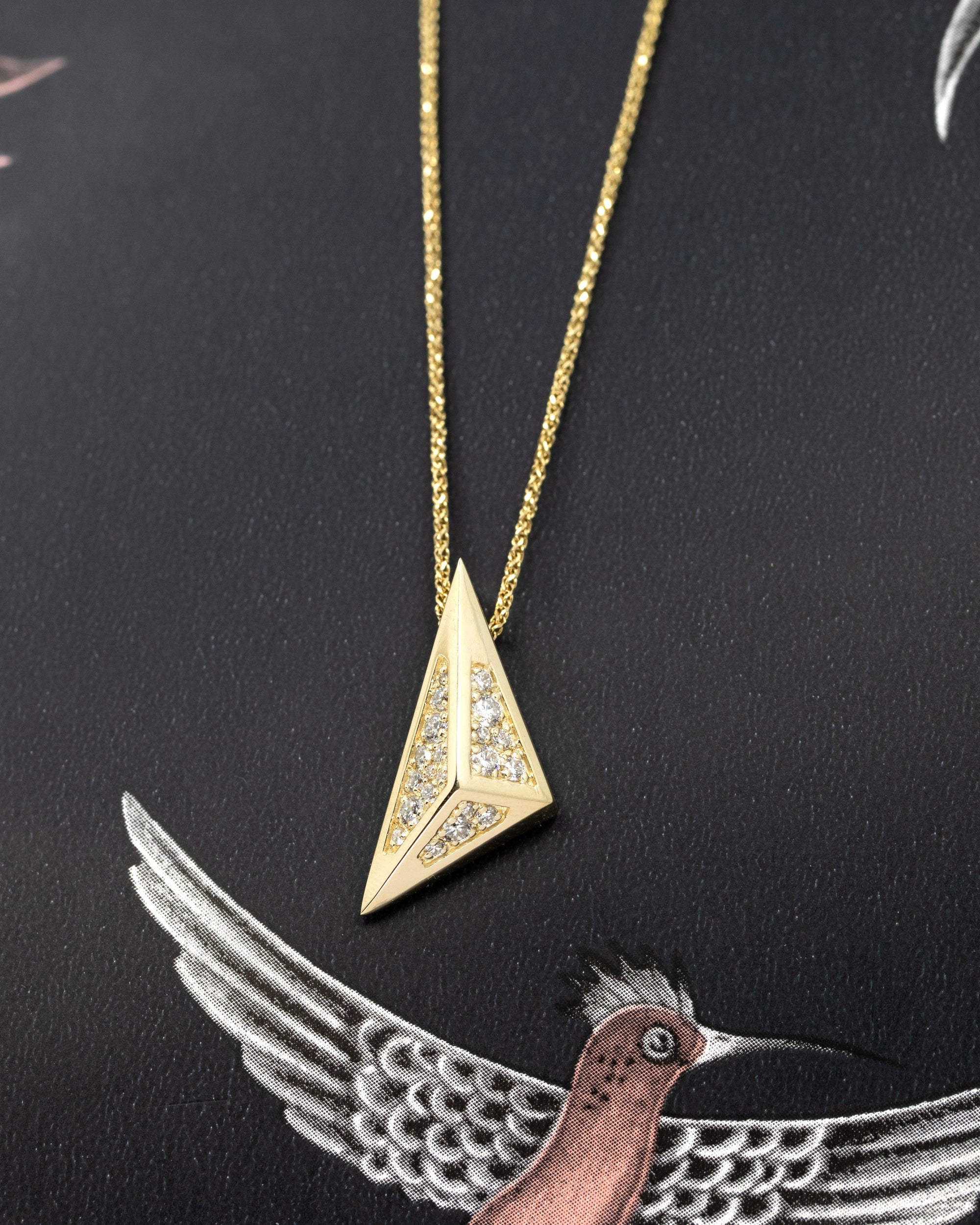 Close-up of the Edgy Pyramidal Pendant in yellow gold, featuring intricate diamond paving and bold triangular lines, set against a sleek black backdrop by Bena Jewelry.