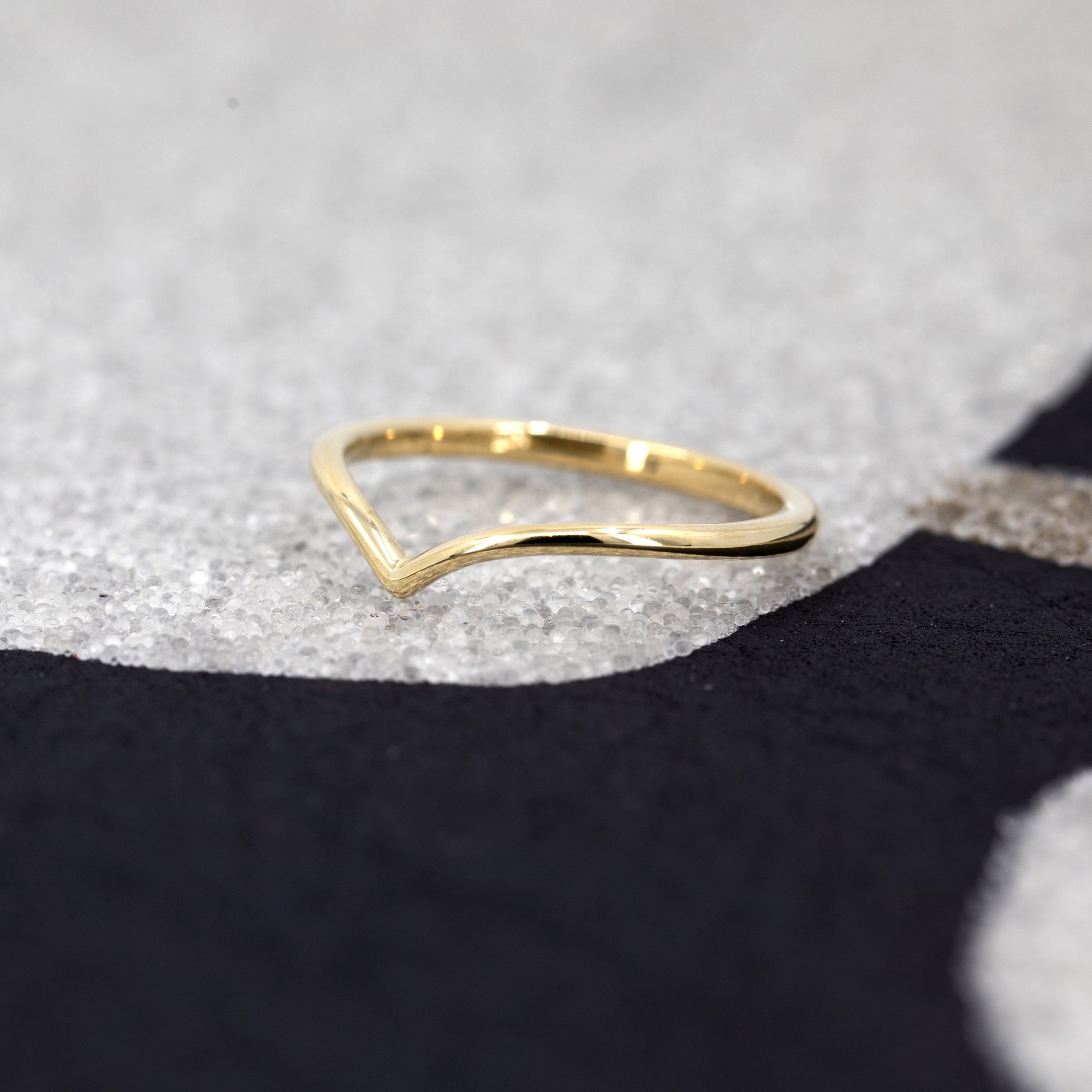 Velar Band by Bena Jewelry, a sleek V-shaped yellow gold wedding ring, showcased on a black background for contrast.