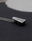 Dramatic close-up of a white gold and diamond pendant necklace, highlighting its bold, faceted design. Bena Jewelry’s signature edgy aesthetic, photographed on a dark background.