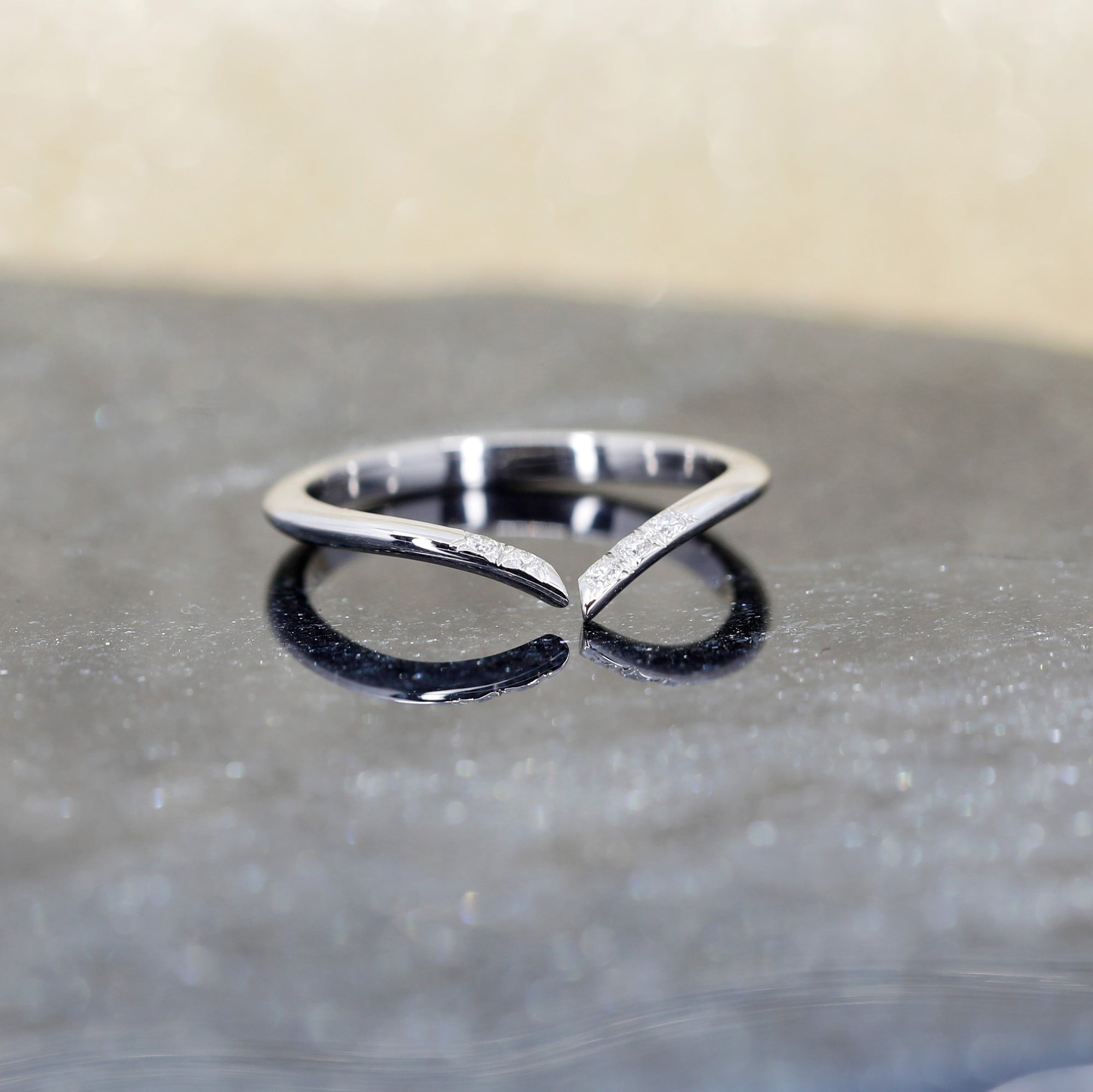 A refined white gold wedding band featuring natural diamonds, showcased on a textured natural black quartz surface with a sparkling gold backdrop that enhances its elegance and brilliance. Designed and handcrafted in Montreal by Bena Jewelry.