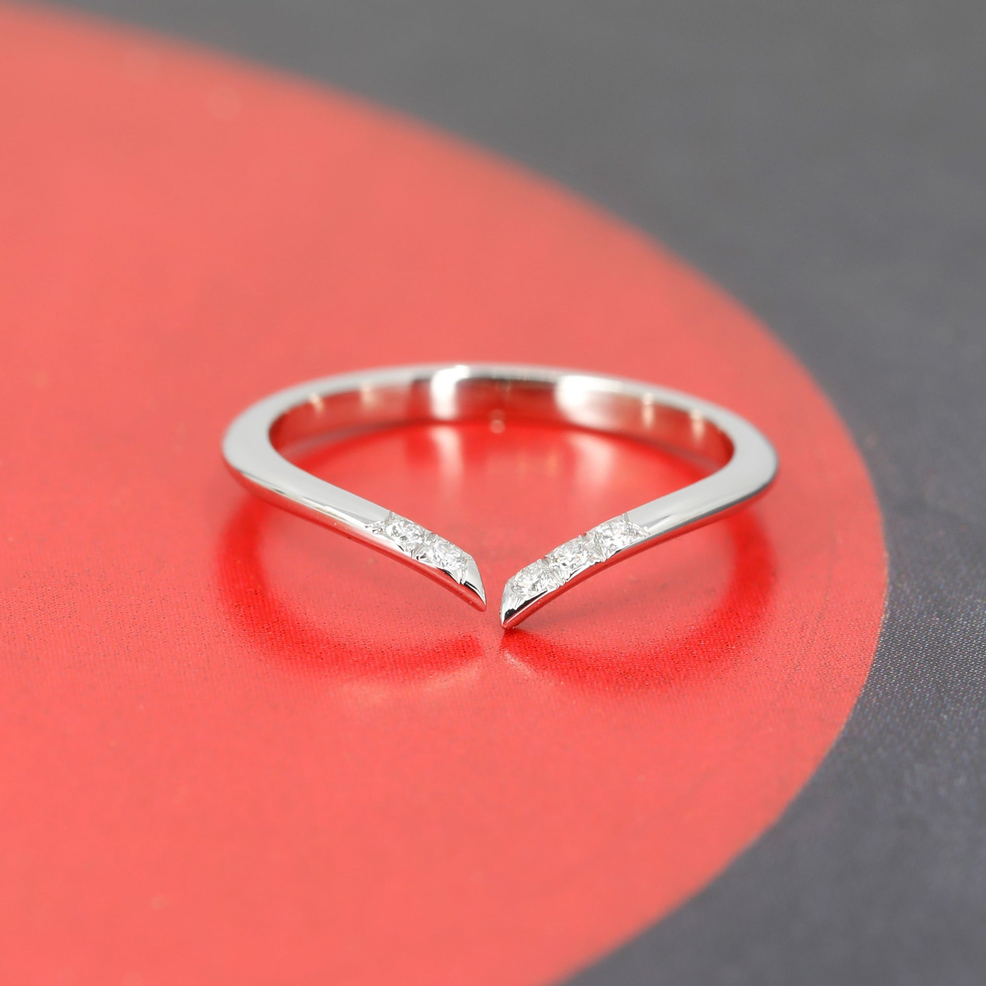 A delicate white gold wedding band with natural diamonds, displayed on a vibrant red circular backdrop, emphasizing its sleek design and the brilliance of the diamonds. A design from Bena Jewelry, an independent Canadian brand.
